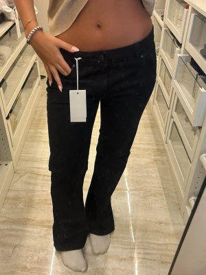 Svarta bootcut jeans - Snygga svarta bootcut jeans med klassisk femficksmodell och hög midja. Jeansen har en stilren look och är perfekta för dig som gillar en tidlös och trendig stil. Materialet ser ut att vara stretchigt och bekvämt, vilket ger en schysst passform.