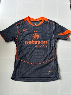 Inter milan tröja - Snygg mörkgrå Inter fotbollströja från Nike med orange detaljer och tryck. Tröjan har korta ärmar, rund hals och logga på bröstet. Tillverkad i lätt och ventilerande material, perfekt för träning eller match.