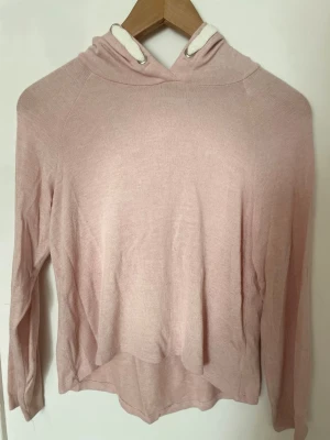 Ljusrosa hoodie med huva - En enkel och mjuk ljusrosa hoodie med lång ärm och huva. Hoodien har vita dragsnören och är tillverkad i ett tunt material🩷