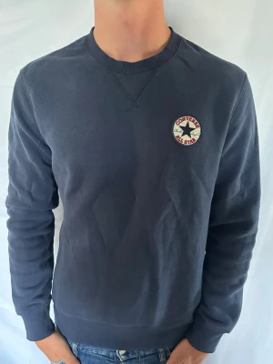Converse tröja  - Mörkblå sweatshirt med rund hals och Converse All Star-logga broderad på bröstet. Tröjan har långa ärmar, ribbade muddar och klassisk passform. Perfekt för en avslappnad stil.