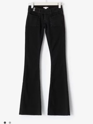 Svarta bootcut jeans med paljettdetalj - Snygga svarta bootcut jeans med två knappar i midjan och stora framfickor. Baksidan har en unik ficka dekorerad med svarta paljetter i ett mönster. Jeansen har utsvängda ben och är tillverkade i ett klassiskt denimtyg. Perfekta för dig som vill sticka ut lite extra.