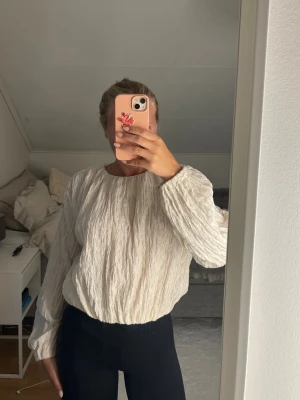 Vit crinkle-blus med lång ärm - Säljer en vit blus med crinkle-effekt och rund hals. Blusen har långa, lösa ärmar och ett avslappnat fall. Från hm och använd 1 gång!