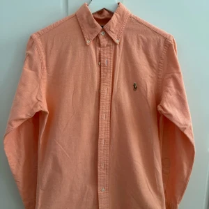 Orange skjorta från Ralph Lauren S - Snygg orange skjorta från Ralph Lauren i slim fit-modell. Skjortan har klassisk krage med knappar, lång ärm och broderad logga på bröstet. Tillverkad i stretchig bomull för extra komfort. 10/10 skick