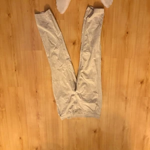 Beige chinos med rak passform - Snygga beige chinos med klassisk rak passform och diskreta fickor. Byxorna har bälteshällor och stängs med knapp och dragkedja. Perfekta för en stilren och avslappnad look. Materialet ser ut att vara bomull, vilket ger en skön känsla. Size 29/32