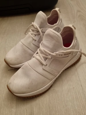 Vita sneakers från U.S. Polo Assn. - Snygga vita sneakers från U.S. Polo Assn. med meshdetaljer och gummisula i brunt. Skorna har klassisk snörning, diskret logga på sidan och guldfärgad polospelare på hälen. Perfekta för en sportig och clean look.