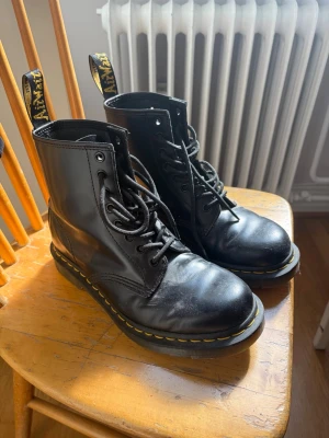 Svarta Dr. Martens boots - Klassiska svarta Dr. Martens boots i läder med gul söm runt sulan. Nästintill oanvända, använda max 5 ggr. Säljer då de ej kommit till användning på ett tag, därav lite dammiga😁 Priset går att förhandla 