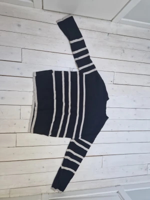 Svart stickad tröja från Vero Moda - Snygg svart stickad tröja från Vero Moda med vita horisontella ränder på både kropp och ärmar. Tröjan har rund halsringning och ribbade muddar. Perfekt för dig som gillar klassiska ränder och enkel stil.
