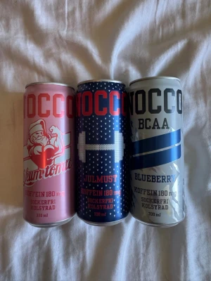 Nocco energidryck 3-pack olika smaker - Tre burkar Nocco energidryck i smakerna Skumtomte (rosa burk med tomte), Julmust (blå burk med vitt mönster) och Blueberry (silverblå burk). Alla är sockerfria, kolsyrade och innehåller 180 mg koffein. Varje burk rymmer 330 ml.