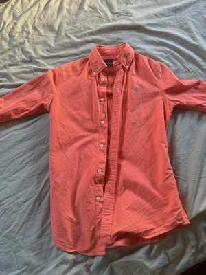 Polo Ralph lauren skjorta  - Snygg korallfärgad skjorta i bomull med klassisk krage och långa ärmar. Skjortan har knappar hela vägen framtill och en liten broderad logga på bröstet. Perfekt för dig som vill ha en färgklick i garderoben.
