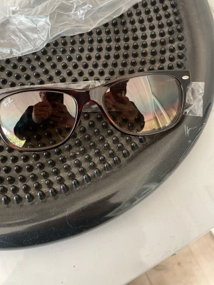 Ray-Ban Wayfarer leopardmönstrade solglasögon - Snygga Ray-Ban Wayfarer solglasögon med klassisk leopardmönstrad båge och mörka glas. Ikonisk design med silverdetaljer vid fronten och Ray-Ban-logga på sidan. Perfekta för dig som vill ha en tidlös och trendig look.