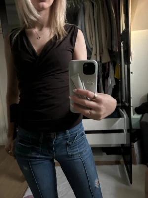 Mörkbrun omlottopp med v-ringning - Snygg mörkbrun omlottopp med v-ringning och ärmlös design. Toppen har en figurnära passform och är perfekt att matcha med jeans eller kjol. Materialet känns mjukt och stretchigt, vilket gör den bekväm att bära hela dagen.