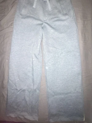 Ljusgrå mjukisbyxor med dragsko - Ljusgrå mjukisbyxor med raka ben och resår i midjan samt dragsko. Byxorna har fickor på sidorna och är gjorda i ett mjukt och bekvämt material, perfekt för chill dagar. Enkel och stilren design som passar till det mesta.