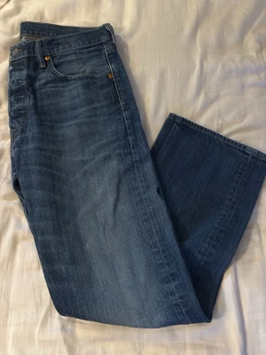 Levi's 501 blå raka jeans - Klassiska blå Levi's 501 jeans med rak passform och fem fickor. Jeansen har en snygg tvättad look och är tillverkade i slitstarkt bomullsmaterial. Perfekta för dig som gillar tidlös denimstil.