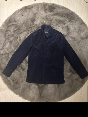 Mörkblå manchester overshirt - Overshirt i mörkblå manchester med klassisk krage, knäppning framtill och en bröstficka. Skjortan har långa ärmar och en rak passform som ger en avslappnad vibe. Perfekt att bära som lager över en t-shirt.