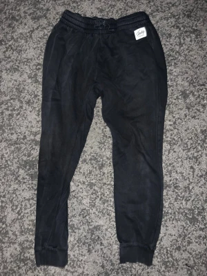 Svarta mjukisbyxor från Frank Dandy - Svarta mjukisbyxor från Frank Dandy med resår i midjan och muddar vid bensluten. Byxorna har en enkel och clean look med en liten vit logga på vänster sida. Perfekta för chill dagar eller när du vill vara bekväm.