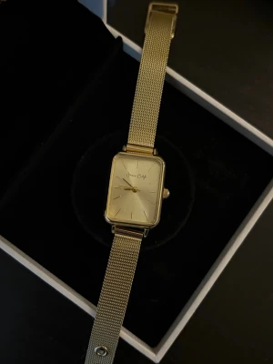 Guldig mesh-klocka med rektangulär urtavla - Stilren klocka i guld med rektangulär urtavla och mesh-armband. Urtavlan har minimalistisk design med tunna visare och index. Armbandet har justerbart spänne och ger en modern känsla. Perfekt accessoar för dig som gillar en clean och unik look 