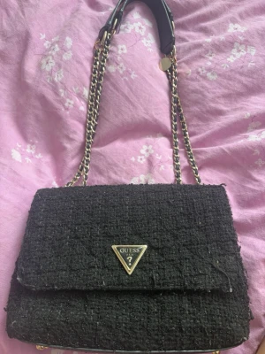 Svart axelväska  från Guess - Väldigt snygg guess väska som är väl andvänd. Den har lite små defekter på bilderna och är liksom ganska andvänd. Men inget man fokuserar jätte mycket på. Den har små slitningar på loggan och är lite trött i materialet. Kolla bilder