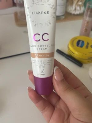 Lumene CC Cream Medium 2 - Lumene CC Color Correcting Cream i nyansen 2 Medium. Ger en jämn hudton med medium täckning och passar alla hudtyper. Innehåller SPF20 och är vegansk. Tuben är vit med lila och beige detaljer samt lila lock.
