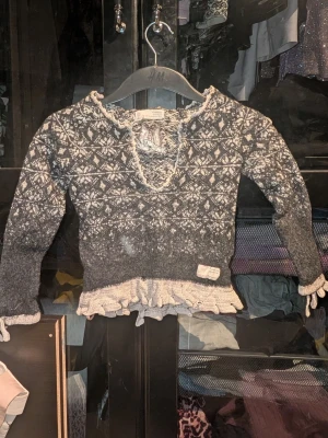 Grå stickad tröja från Odd Molly med mönster - Mysig grå stickad tröja från odd Molly med vitt nordiskt mönster och volangkant nedtill. Tröjan har lång ärm med rosetter, v-ringning och dekorativa detaljer i vitt. Inga synliga fläckar eller defekter. Skapa en bundle för bättre pris