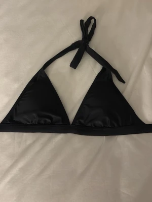 Svart trekantsbikini  - Snygg svart trekantsbikini med knyt i nacken och smidig spänne i ryggen. Klassisk och stilren modell som passar perfekt till stranden eller poolen. Tillverkad i mjukt och stretchigt material för skön passform. Passar även XS