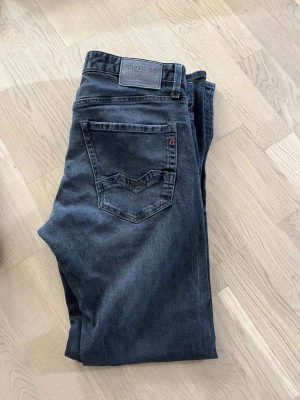  jeans Replay - Snygga mörkgrå jeans från Replay de är i storlek 33-32 med raka ben och klassiska bakfickor med V-formad söm. Jeansen har en diskret Replay-logga på bakfickan och är tillverkade i mjukt denimtyg. Perfekta för en avslappnad och trendig look.