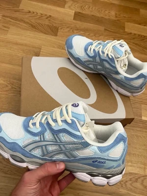 Asics GEL-NYC blå och vita sneakers - Excellent condition ASICS sneakers in a beautiful light blue and white colorway. Comfortable, stylish, and perfect for everyday wear. ✅ Original box included ✅Original receipt included ✅ Clean and well maintained ✅Ready to ship These sneakers combine comfort and sporty style, making them ideal for casual outfits, walking, or daily use. Feel free to contact me if you have any questions or would Like more photos.