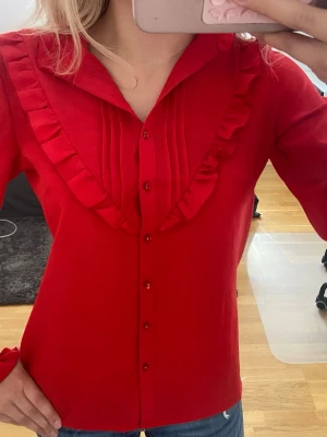 Röd blus - Säljer denna jättefina röda blus med knappar och volang detaljer. Jag har köpt den secondhand men den är fortfarande i jättefint skick. Jag vet tyvärr inte märket, men storleken är 38, passar 36 och 34 också för en lösare passform.