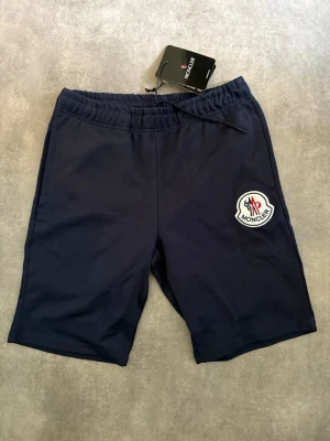 Mörkblåa shorts med märke på. - Mörkblåa shorts med märke på. Mjuka som mjukisbyxor. Fickor på sidorna. Resår och snören i midjan. Aldrig använda, lapp kvar.