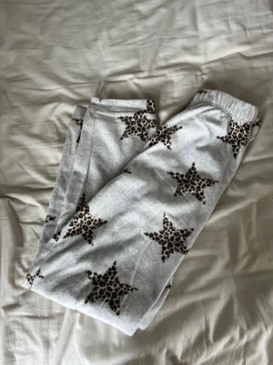 Gråa mjukisbyxor med stjärnmönster - Mysiga gråa mjukisbyxor med leopardmönstrade stjärnor. Byxorna har resår i midjan och är perfekta för chill dagar hemma. Materialet ser ut att vara mjukt och skönt, perfekt för loungewear.