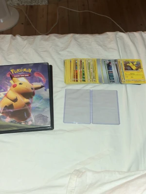 68st holo kort i bulk+ four pocket binder+ toploaders. - 68 olika holografiska / glittriga kort från alla olika år 2013-2026, helt okej skick på dom. du får med en four pocket pärm med v max pikachu och zarude på omslaget, mystery cards i pärmen, och du får 2 toploaders.