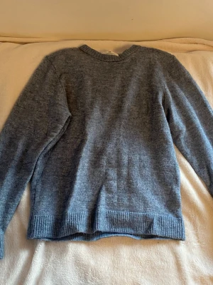Blå stickad tröja från H&M - Mysig blå stickad tröja från H&M med rund halsringning och ribbade muddar vid ärmslut och nederkant. Perfekt för lager på lager och enkel att matcha med olika outfits. Materialet känns mjukt och bekvämt.