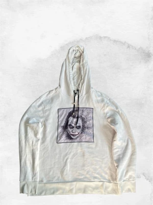 Vit hoodie med tryck från Limitato - Vit hoodie från Limitato med stor huva och justerbar dragsko. På bröstet finns ett svartvitt tryck av ett ansikte i fyrkantig ram. Raka ärmar och breda muddar vid ärmslut och nederkant. Materialet ser ut att vara mjuk bomull.