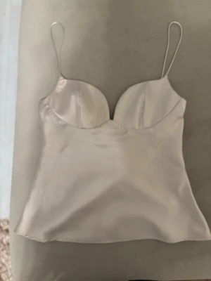 Champagnefärgad satinlinnetopp Zara - Snygg champagnefärgad linnetopp från Zara i satin med tunna axelband och formade kupor. Perfekt för att skapa en trendig och stilren look. Lätt glansigt material som ger en lyxig känsla. Så söt! Har tagit bort prislappen men den är köpt på plick och aldrig använd!!❣️