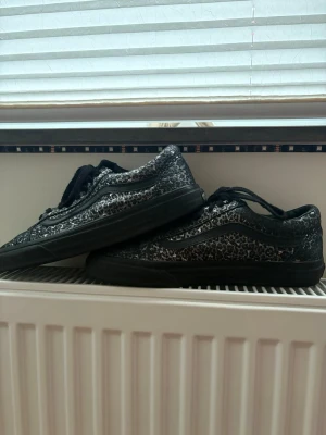 Svarta VANS sneakers med leopardmönster - Säljer ett par svarta sneakers med coolt leopardmönster och svarta snören. Skorna har en låg profil och svart sula. Mycket väl omhändertagna!!