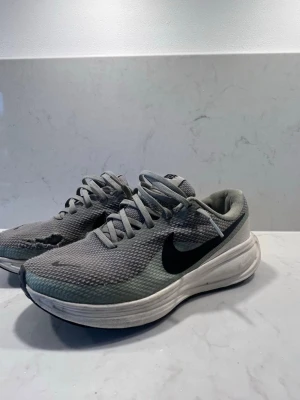 Grå Nike sneakers med svart swoosh - Snygga grå sneakers från Nike med svart swoosh på sidan. Ovandelen är i meshmaterial för bra andningsförmåga och sulan är vit med en sportig look. Perfekta för dig som gillar en clean och enkel stil.