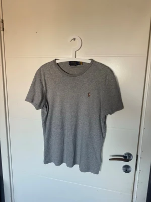 Grå t-shirt från Polo Ralph Lauren - Snygg grå t-shirt från Polo Ralph Lauren i custom slim fit. Klassisk design med korta ärmar och rund halsringning. Liten broderad logga på bröstet. Perfekt basplagg i mjuk bomull som passar till allt.