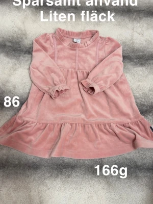 Rosa mjuk klänning med volang - Supersöt rosa klänning i mjukt material med lång ärm och volangkant nedtill. Klänningen har en enkel design med rund hals och resår vid ärmsluten för extra komfort. Perfekt för dig som gillar en gullig och bekväm stil.🌸 Sparsamt använd. En liten fläck. Storlek 86