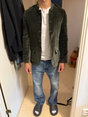 Limitato kavaj - Snygg olivgrön kavaj i suede från Limitato med fyra knappar framtill och två stora fickor med lock. Storleken är m men den sitter som s-m. Kavajen är i slim fit. Knappen längst ner saknas och det är den ända defekten på kavajen. Modellen är 176cm och väger 72 kg. Nypris: 4500