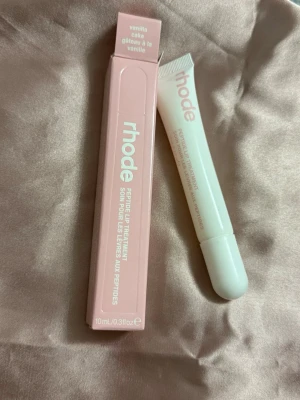 Rhode Peptide Lip Treatment Vanilla - Rhode Peptide Lip Treatment i doften Vanilla Cake. Kommer i en stilren vit tub med rosa förpackning. Läppbalsamet är berikat med peptider för att återfukta och ge mjuka läppar. Perfekt för dig som vill ha ett lyxigt och vårdande läppbalsam.