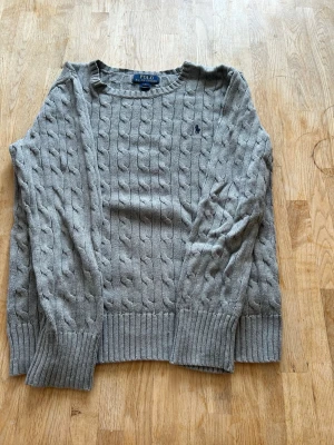 Grå kabelstickad tröja Polo Ralph Lauren - Barn storlek L motsvarar Xs. Defekt som syns i bilden, behövs bara sy ihop 