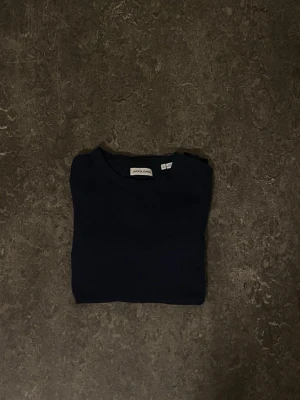 Mörkblå tröja från Jack & Jones - En enkel och stilren mörkblå tröja från Jack & Jones. Tröjan har rund halsringning och långa ärmar, perfekt för lager på lager eller att bära som den är. Passar till det mesta och är ett måste i garderoben.