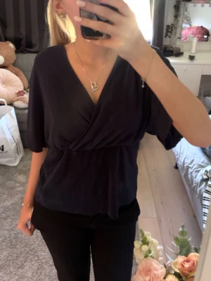 Mörkblå omlottopp med v-ringning - Säljer en mörkblå omlottopp med v-ringning och korta, lösa ärmar. Perfekt att styla med både jeans och kjol. Bara använt en gång. Pris kan alltid diskuteras!                                                                  (Det är inte en rosa fläck bak på toppen utan det är ljuset🥹) 