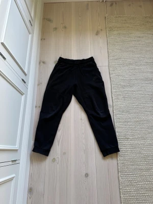 Svarta Nike Tech byxor - Säljer ett par svarta Nike Tech mjukisbyxor med resår i midjan och muddar vid bensluten. Byxorna har en avslappnad passform och är tillverkade i ett mjukt material, perfekta för chill dagar. Ena bakfickan har dragkedja för extra funktion. Köptes på unisport förra året för 599 säljs nu för 249 för att dem inte används längre. Perfekt för dig som vill ha ett par billiga och fina mjukisbyxor i storlek 147-158cm.   Bara att höra av sig vid bilder eller frågor! Priset kan diskuteras!