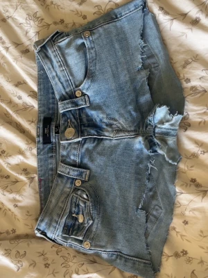 Ljusblå jeansshorts från True Religion - Säljer ett par ljusblå jeansshorts från True Religion med råa, fransiga kanter och klassiska fickor både fram och bak. Shortsen har silverfärgade knappar och en ikonisk patch bak. Perfekta för sommaren! Det är dock ett par jeans i modellen Joey som jag gjorde om till shorts! Pris kan diskuteras såklart 