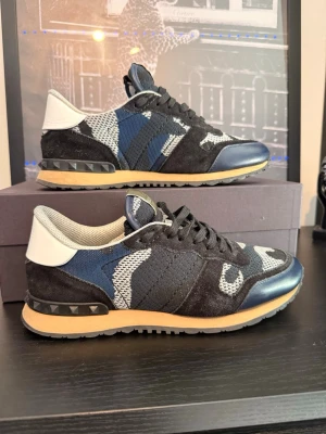 Valentino Garavani camo sneakers - Snygga sneakers från Valentino Garavani med camomönster i svart, blått, vitt och grått. Skorna har detaljer i mocka och läder, vita hälpartier och nitar på sulan. Yttersulan är beige och svart, och skorna har svarta skosnören. Skorna är i toppskick, inga hål eller andra slitage. Box samt dustbag medföljer ej🤩 priset är ej hugget i sten✅skriv vid minsta lilla fundering😁