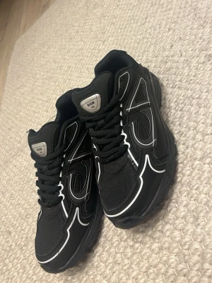 Svarta Dior sneakers med vita detaljer - Snygga svarta Dior sneakers med vita kontrastlinjer och meshpaneler för extra andningsförmåga. Skorna har en chunky sula och klassisk snörning. Perfekta för dig som vill ha en stilren men ändå unik look.