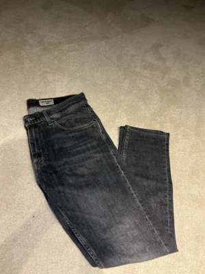 Mörkgrå raka jeans - Säljer ett par mörkgrå jeans med rak passform och klassisk femficksdesign. Jeansen har bälteshällor och knappgylf. Materialet är denim i bomull och de har en snygg tvättad look.