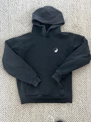 Svart hoodie från Stüssy med logga - Svart hoodie från Stüssy med klassisk stor logga i vitt på ryggen och en liten logga på bröstet. Hoodien har huva, känguruficka och ribbade muddar. Perfekt för en streetwear-look och riktigt skön att bära.