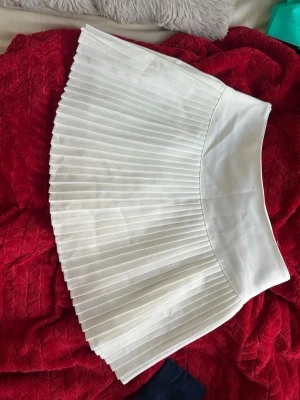 Vit plisserad skort Asian M men passar Eu S - Supersnygg vit skort med plisserad kjoldel och inbyggda shorts. Hög midja och klassisk tenniskjol-look. Tillverkad i ett lätt och mjukt tyg som ger en fräsch och sportig vibe. Perfekt för dig som vill ha kjolkänsla men ändå känna dig bekväm. 