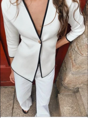 Zara kofta - Stilren vit kavaj med svart kant längs krage och öppning. Kavajen har en djup v-ringning, trekvartsärmar och stängs med en knapp framtill. Passar perfekt till både byxor och kjol för en snygg look.